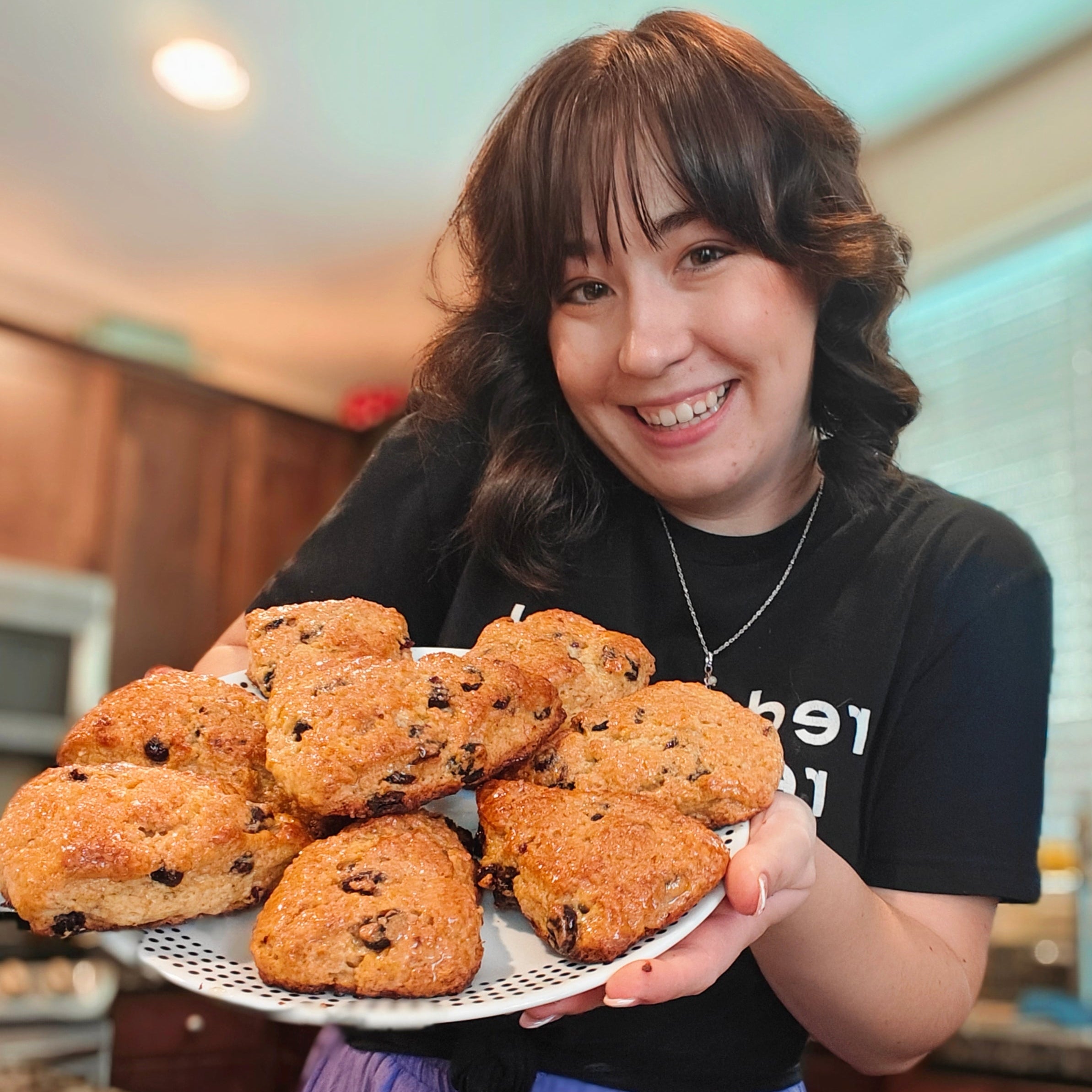 Person holding a plate of scones in a kitchen setting